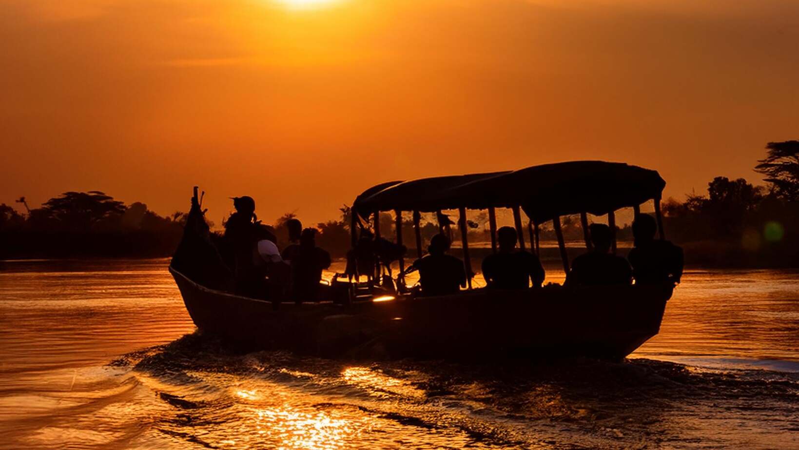 Silhouette d'un chaland sur le lac de Tsiribihina à Madagascar. Coucher de soleil orangé. 7 personnes hétérogènes à bord du bateau