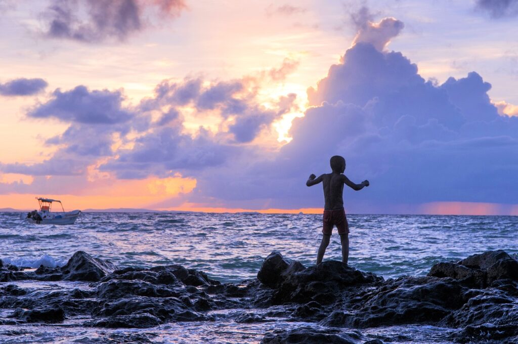 Silhouette d'un garçon de 10 ans vue de dos, jouant sur un rocher au bord de la mer de Sainte Marie