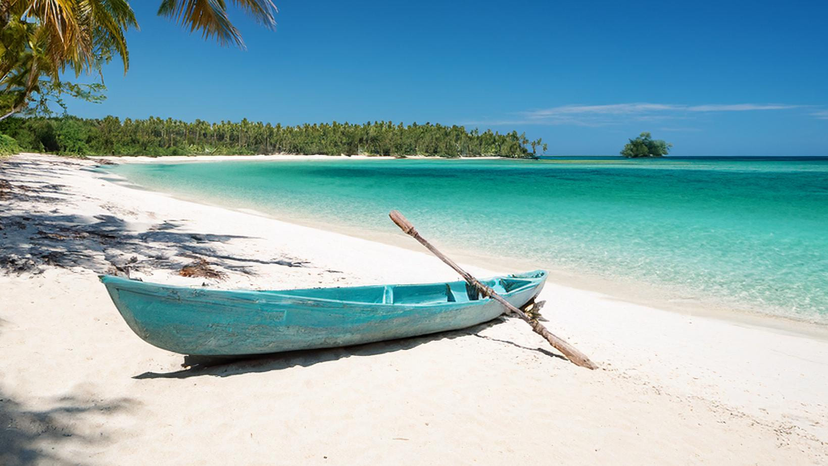 Pirogue de pêche de couleur bleue sur le sable blanc d'une plage au sud de Madagascar. Mer turquoise, fôret de cocotier et ciel bleu en fond.